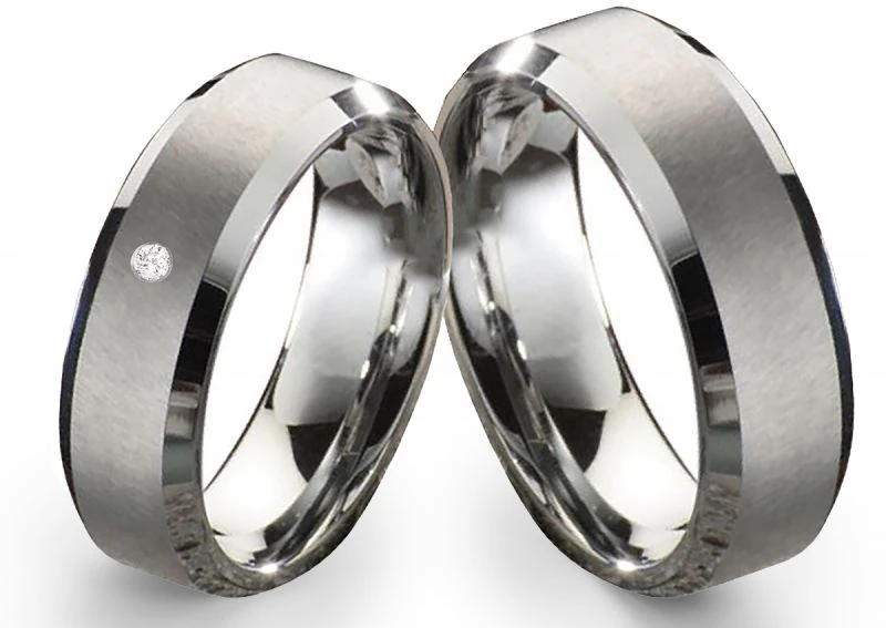 Zwei Wolframringe nebeneinander auf weißem Hintergrund. Die Ringe haben eine mattierte Außenfläche mit polierten Kanten und sind teils glänzend. In einem der Ringe ist ein kleiner, runder Stein (Zirkonia) eingelassen.